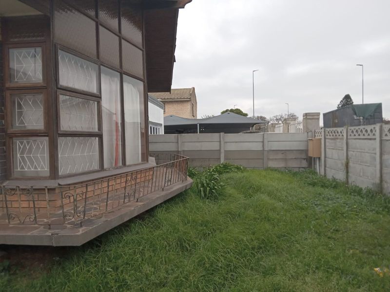 Rear exterior view showing a raised patio with wrought iron balustrade, large bay windows, and a precast concrete boundary wall.