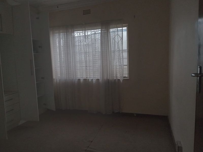 An empty bedroom featuring built-in cupboards, carpeted flooring, and a window fitted with security bars.
