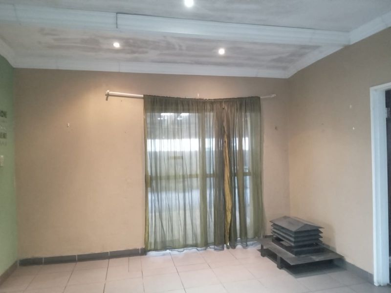 An empty living room featuring tiled flooring, recessed downlights, and a sliding glass door with a curtain rod, ready for staging.