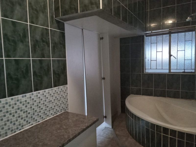 A functional bathroom featuring a built-in corner bathtub, tiled wall finishes, and a vanity countertop, offering a solid foundation for modernization.