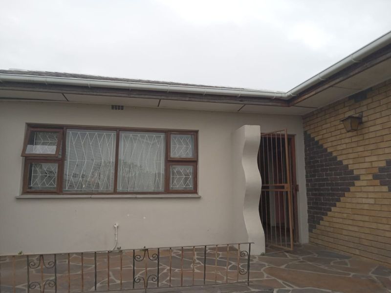 Rear exterior view featuring a stone paved patio, brick accent wall, and security gate access to the building.