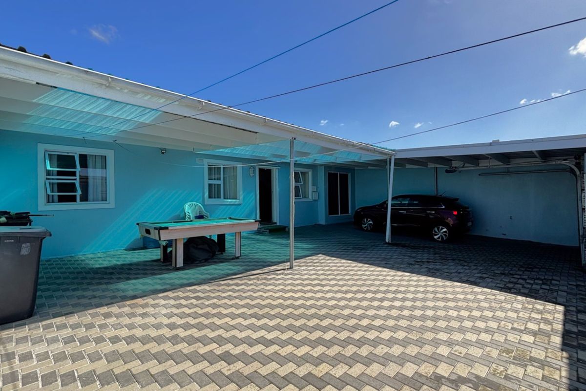 A paved rear courtyard area featuring a covered patio space and an integrated carport, providing functional outdoor living and parking utility.