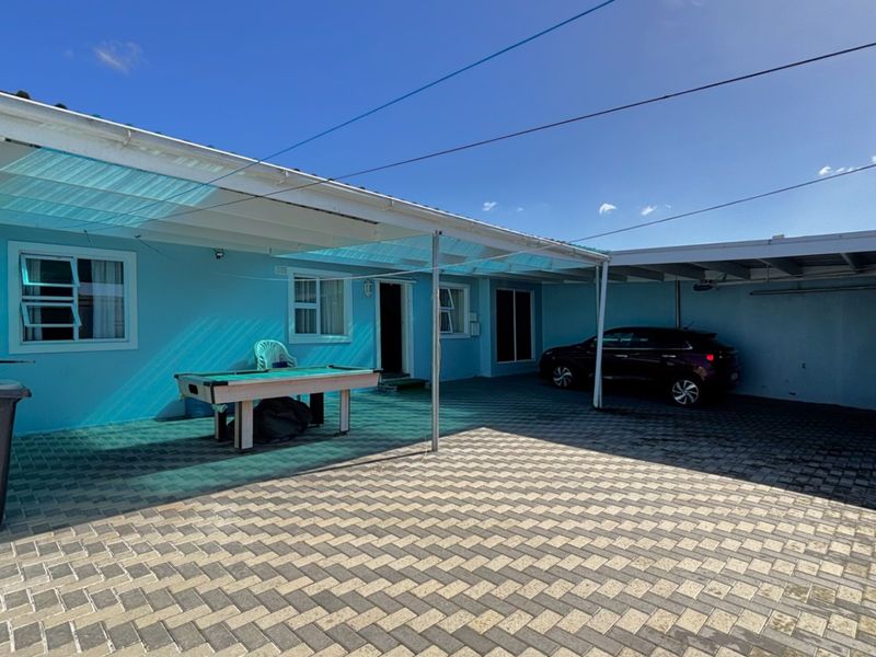 A paved rear courtyard area featuring a covered patio space and an integrated carport, providing functional outdoor living and parking utility.