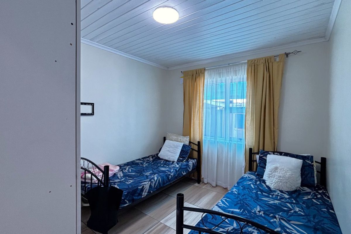 A functional bedroom featuring timber-look floor tiles and a classic tongue and groove ceiling, providing a simple and practical living space.
