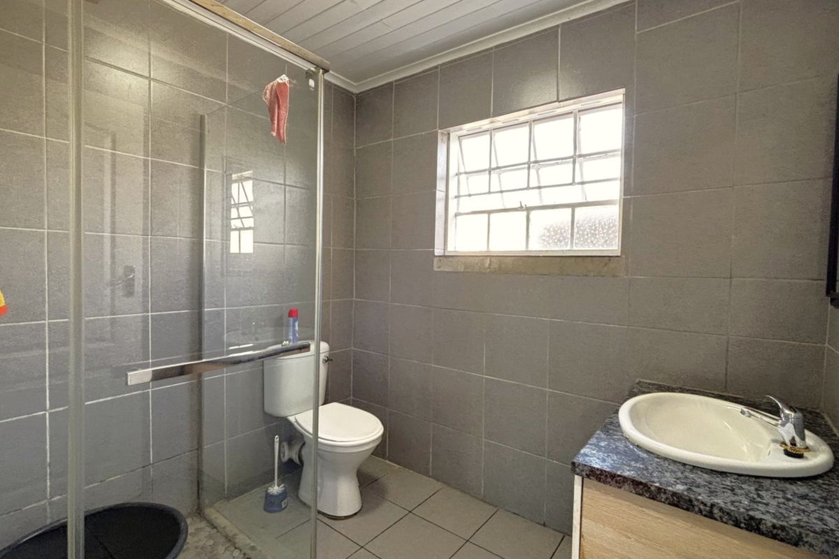 A functional bathroom featuring a glass-enclosed shower, a vanity with a stone countertop, and full-height wall tiling.