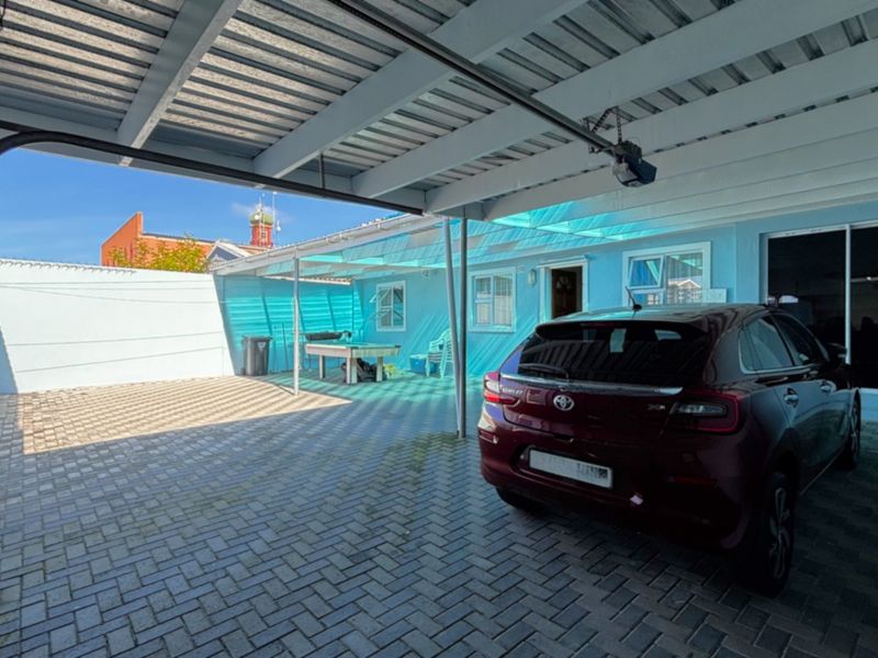 A covered outdoor parking area featuring paved flooring, a corrugated metal roof, and direct access to the main dwelling via a sliding door.