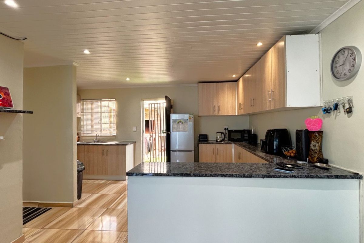 Functional kitchen featuring granite countertops, light wood-finish cabinetry, tiled flooring, and recessed lighting, with an open-plan layout leading to an exterior door.