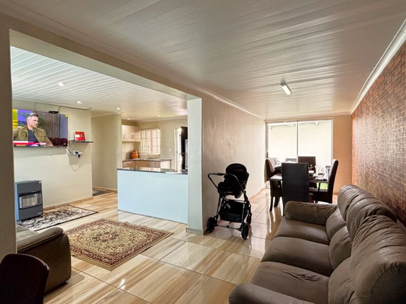 Spacious open-plan living and dining area featuring tiled floors, a brick feature wall, and a connected kitchen with functional cabinetry.