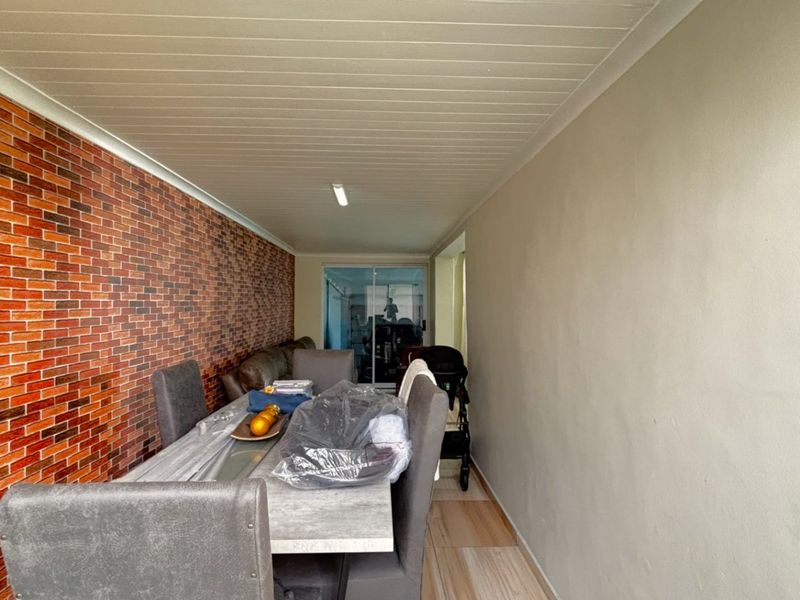 A covered patio area featuring a decorative brick-style feature wall, tiled flooring, and a tongue and groove ceiling, providing a functional outdoor living space.