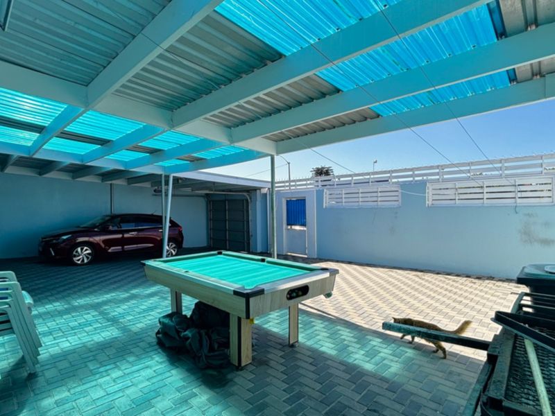 A spacious covered outdoor patio area featuring paved flooring and a translucent blue corrugated roof, suitable for entertainment or vehicle storage.