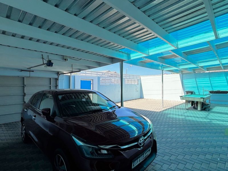 A spacious covered outdoor patio area featuring paved flooring, a corrugated metal roof with translucent panels, and an integrated garage entrance.