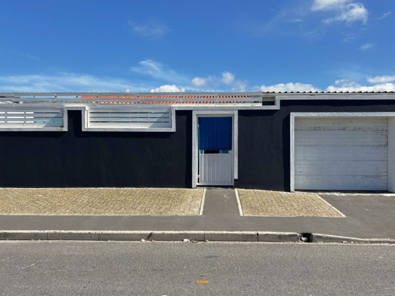 Front facade featuring a dark-painted perimeter wall with security spikes, a single pedestrian gate, and a private garage entrance with paved driveway access.