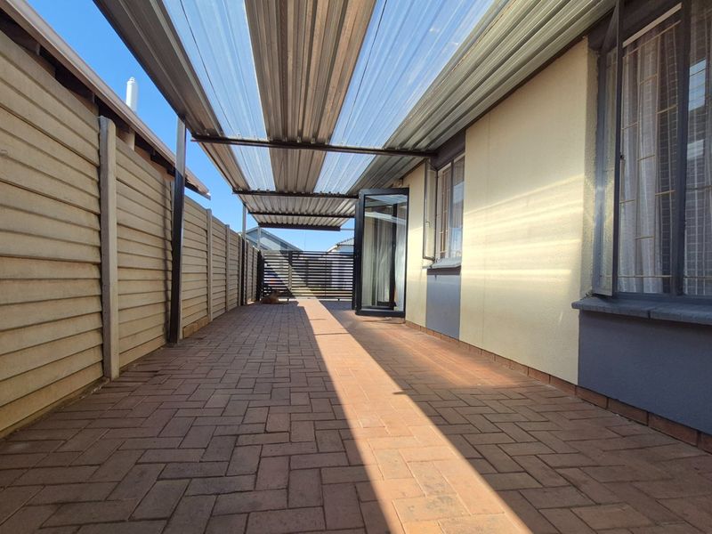 A covered outdoor patio area featuring paved flooring, a corrugated roof, and secure boundary walls, providing a functional space for outdoor living.