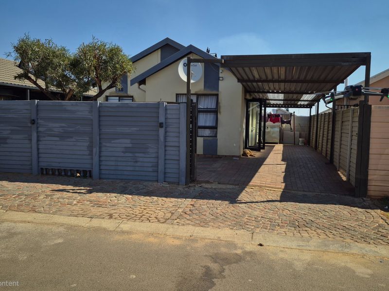 Front exterior view of the property featuring a paved driveway, a covered carport, and a secure boundary wall.