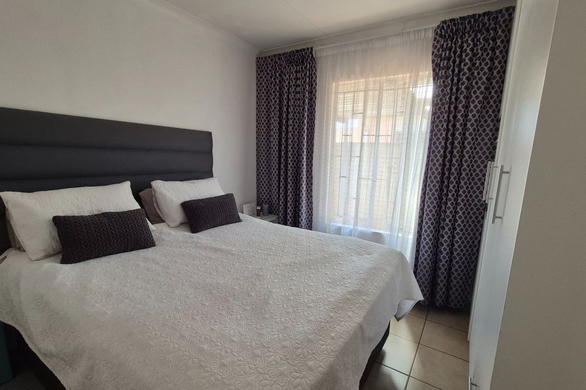 A well-maintained bedroom featuring tiled flooring, a built-in wardrobe, and security bars on the window.