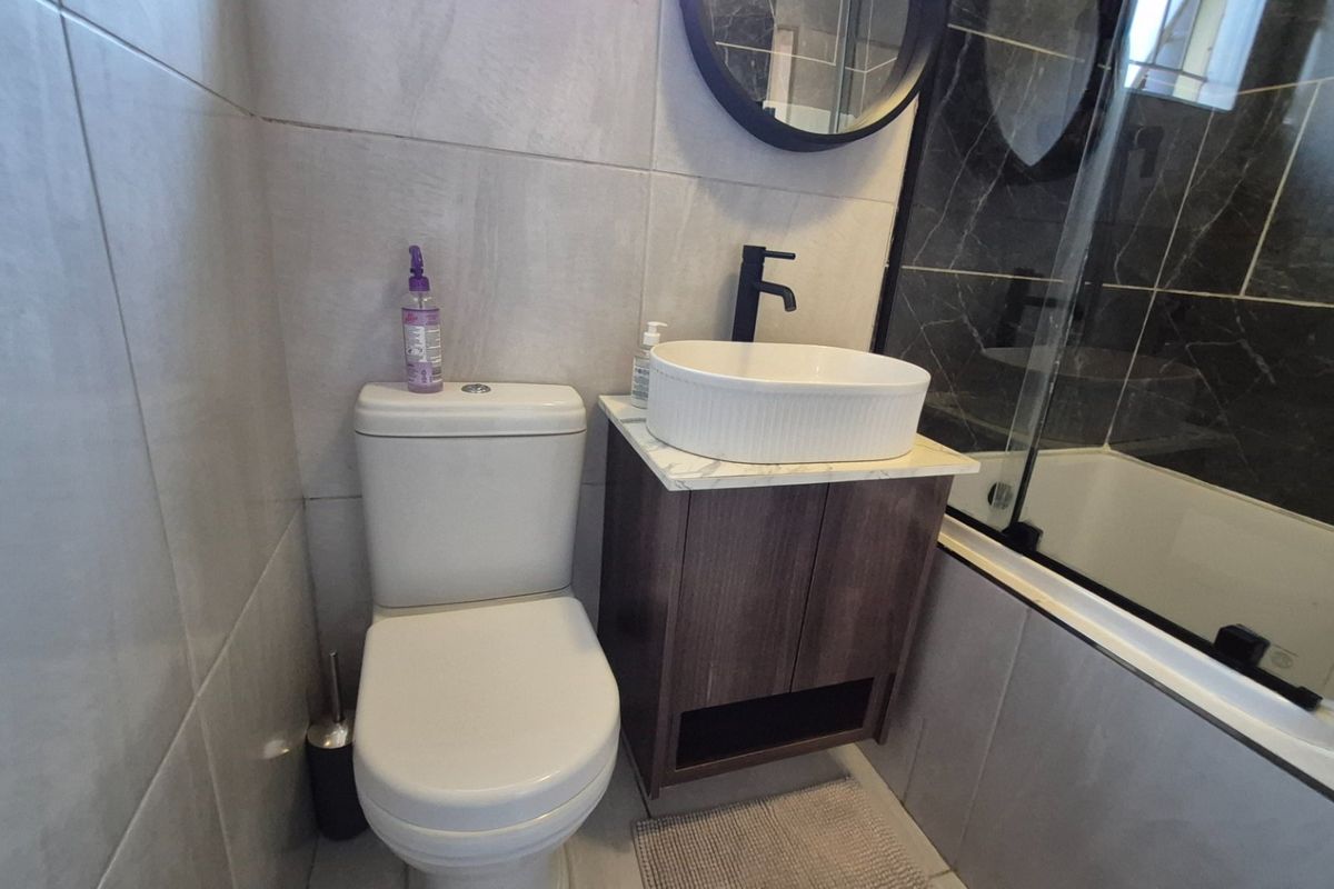 Modern bathroom featuring a vanity cabinet with a vessel sink, black fixtures, and a glass shower screen with tiled finishes.