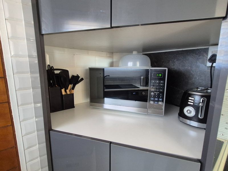 A modern kitchen nook featuring grey cabinetry, a white subway tile backsplash, and a dark stone-look accent panel.