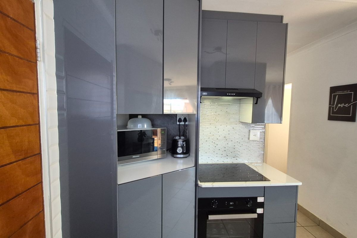 Modern kitchen featuring sleek grey cabinetry, integrated oven, electric hob, extractor fan, and a stylish tiled backsplash with stone countertops.