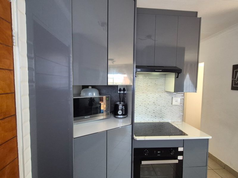 Modern kitchen featuring sleek grey cabinetry, integrated oven, electric hob, extractor fan, and a stylish tiled backsplash with stone countertops.