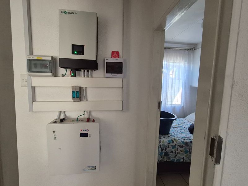 Utility area featuring a wall-mounted solar inverter and lithium battery system for off-grid power management.