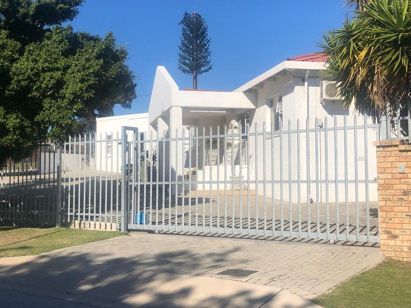 Front exterior view of a commercial property featuring a secure steel gate, paved driveway, and white painted facade with an installed air conditioning unit.