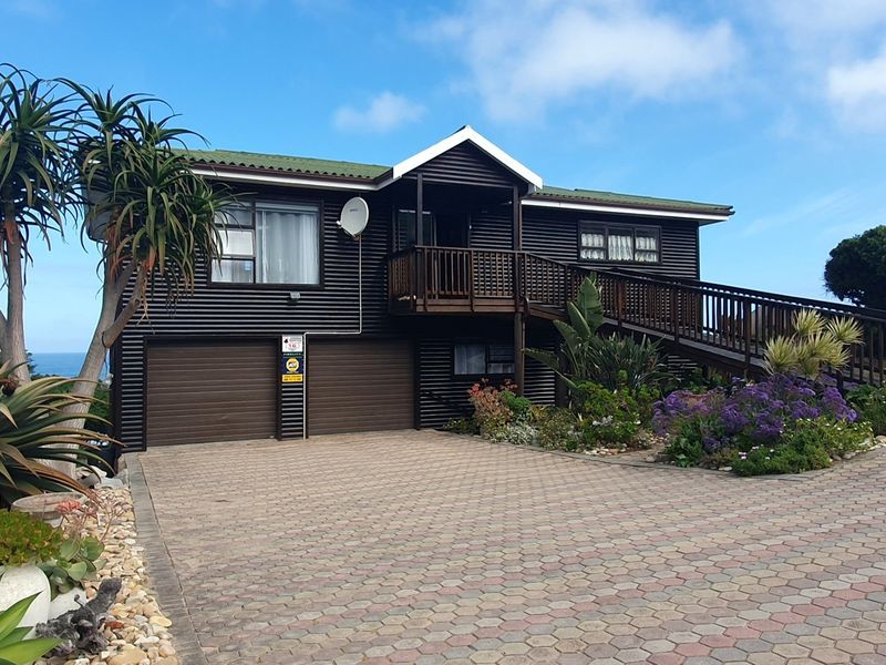 A well-maintained house featuring dark corrugated metal cladding, a paved driveway, double garage, and a raised wooden deck with an accessible ramp.
