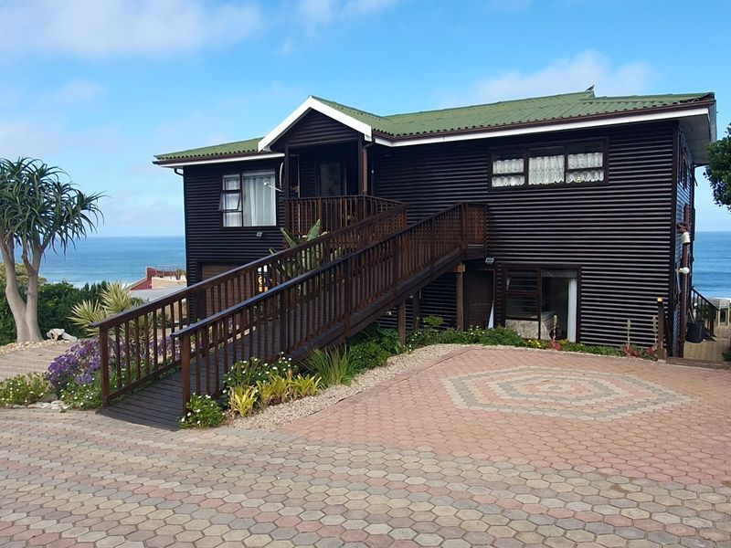 A well-maintained timber-clad house featuring a prominent wooden ramp entrance, paved driveway, and scenic ocean views.