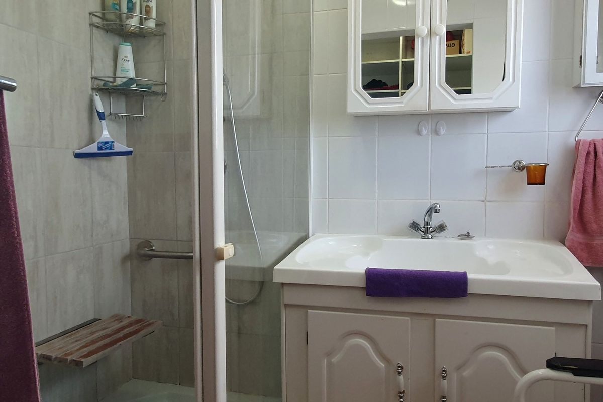 A functional bathroom featuring a shower enclosure with a grab bar, a vanity cabinet with a washbasin, and wall-mounted storage cabinetry.