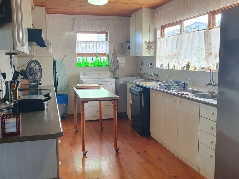 A functional kitchen featuring timber flooring, wood-paneled ceiling, laminate cabinetry, and a double basin sink with tiled splashbacks.