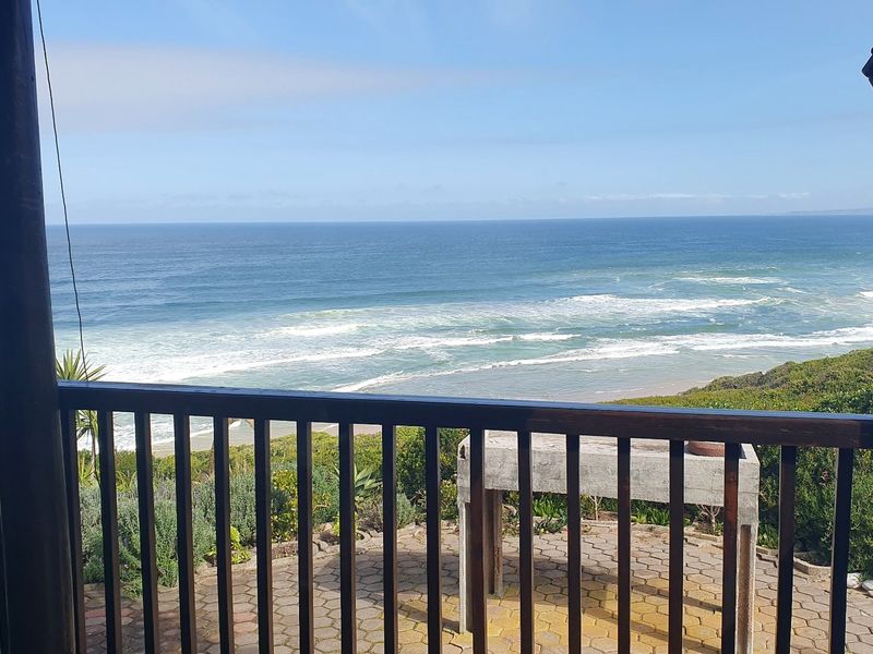 Covered patio featuring a built-in concrete braai and wooden balustrade, offering expansive, unobstructed ocean views.