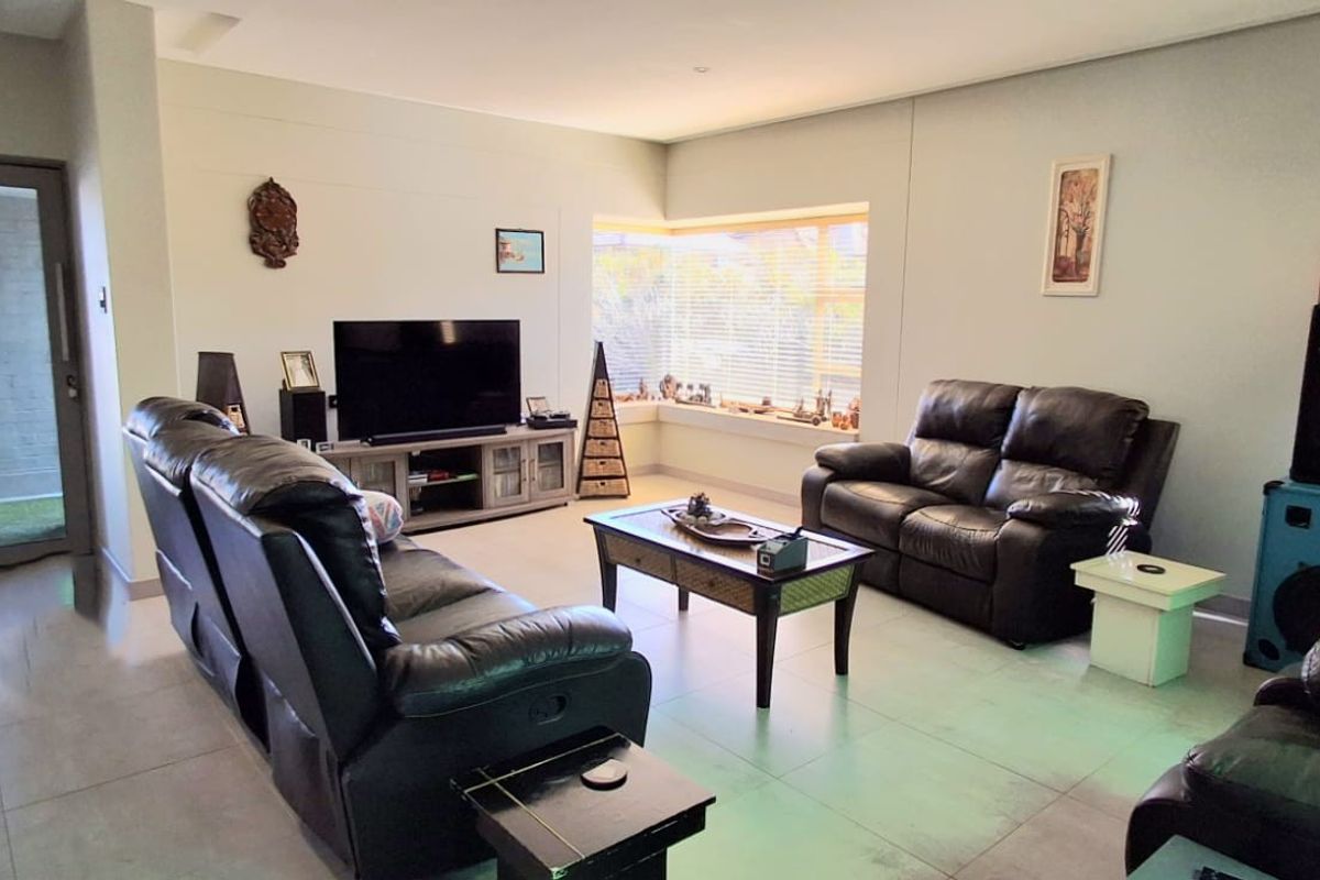 A spacious living room featuring large format floor tiles, recessed ceiling lighting, and a sliding glass door providing access to the exterior.