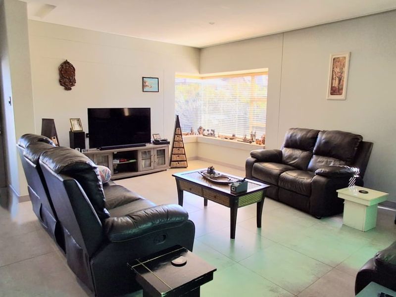 A spacious living room featuring large format floor tiles, recessed ceiling lighting, and a sliding glass door providing access to the exterior.