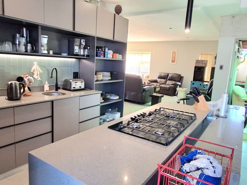 Modern open-plan kitchen featuring a central island with gas cooktop, stone countertops, and seamless cabinetry, flowing into the living area and outdoor patio.