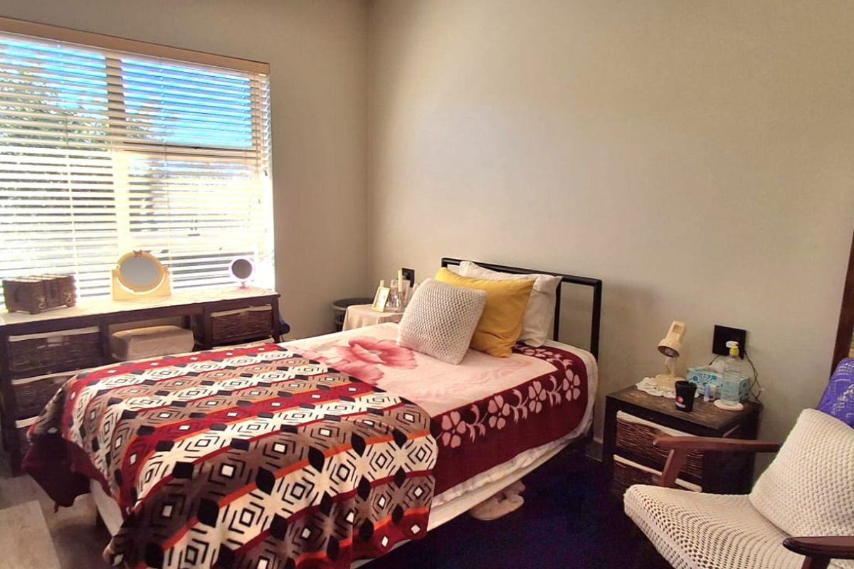 A functional bedroom featuring a large window with venetian blinds and a built-in wardrobe, providing a comfortable and well-lit living space.