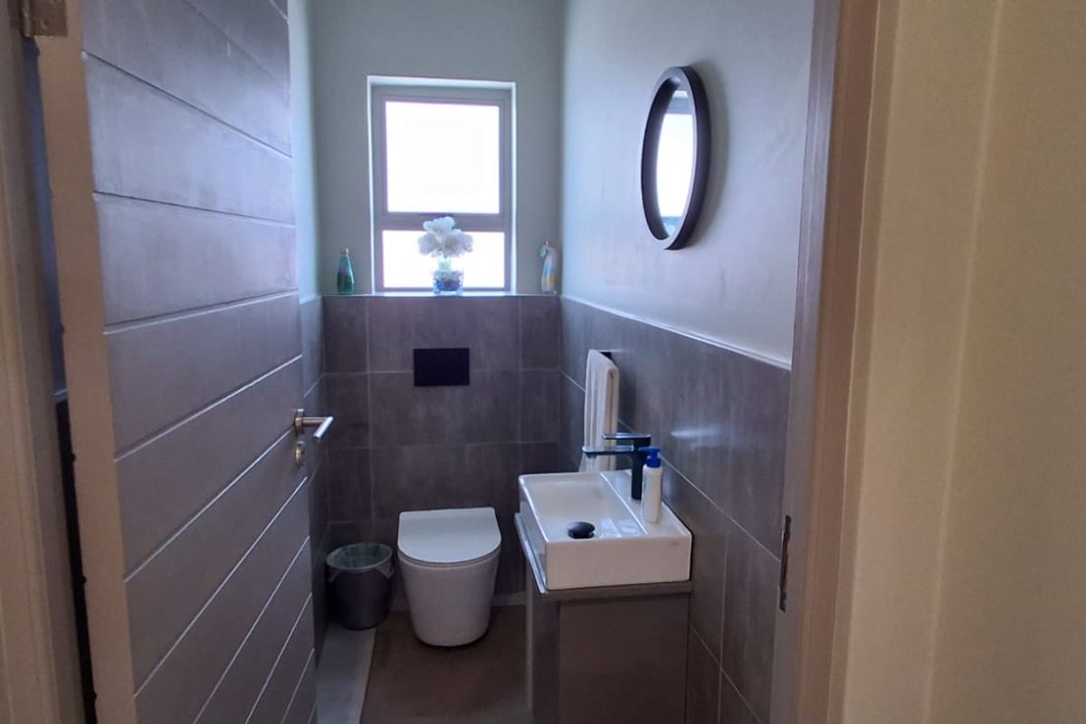 A compact, modern guest bathroom featuring a wall-hung toilet with a concealed cistern, a vanity basin, and neutral wall tiling.