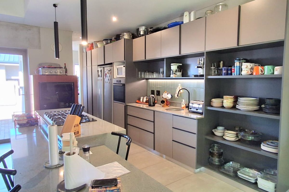 Modern kitchen featuring a large island with gas hob, extensive built-in cabinetry, stone countertops, and integrated appliances with open shelving for storage.