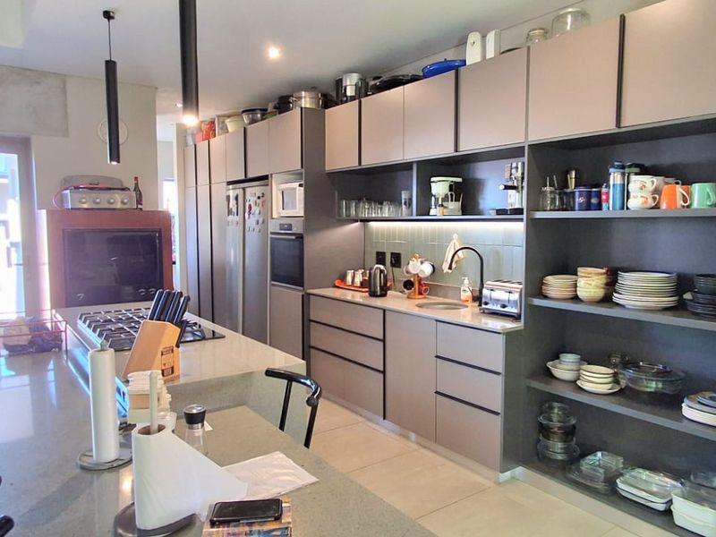 Modern kitchen featuring a large island with gas hob, extensive built-in cabinetry, stone countertops, and integrated appliances with open shelving for storage.