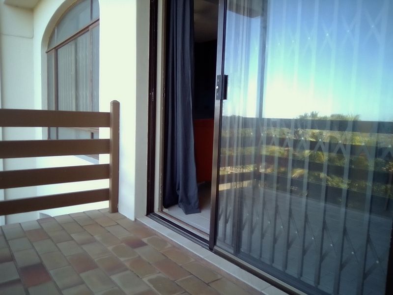 A covered balcony featuring tiled flooring, a sliding glass door with a security gate, and a protective railing.