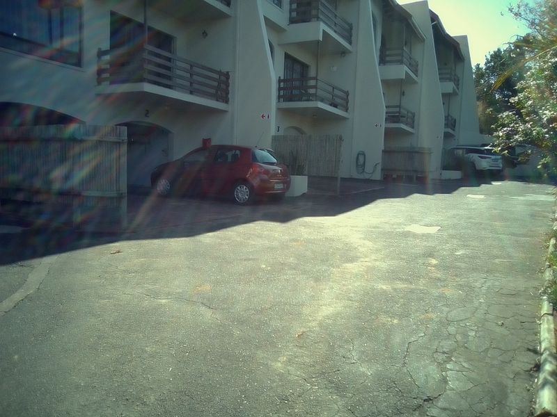 Front exterior view of a townhouse complex featuring a shared asphalt driveway, multi-level balconies, and external building structures.