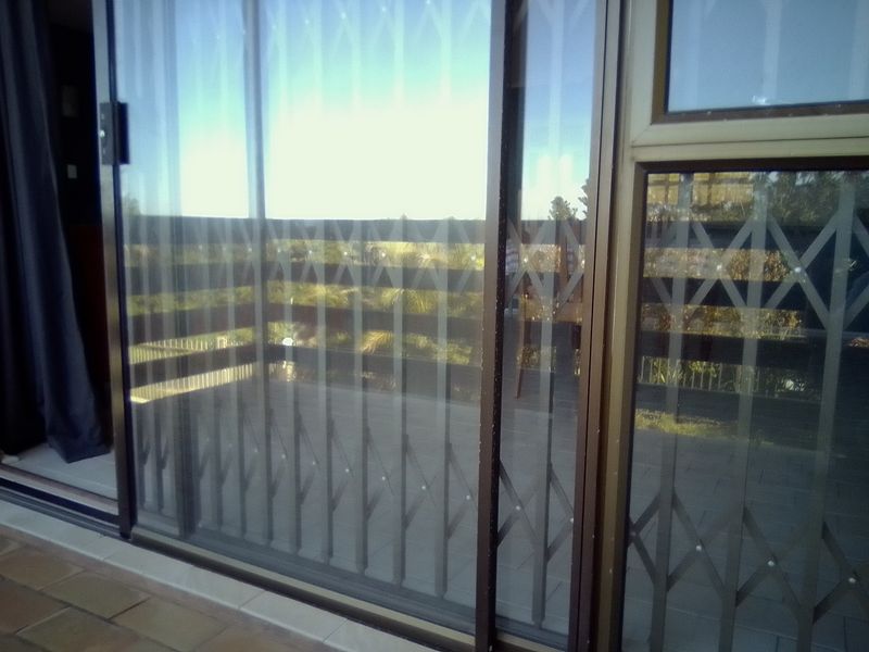 A view through a sliding glass door with a security gate onto a tiled balcony with a railing.