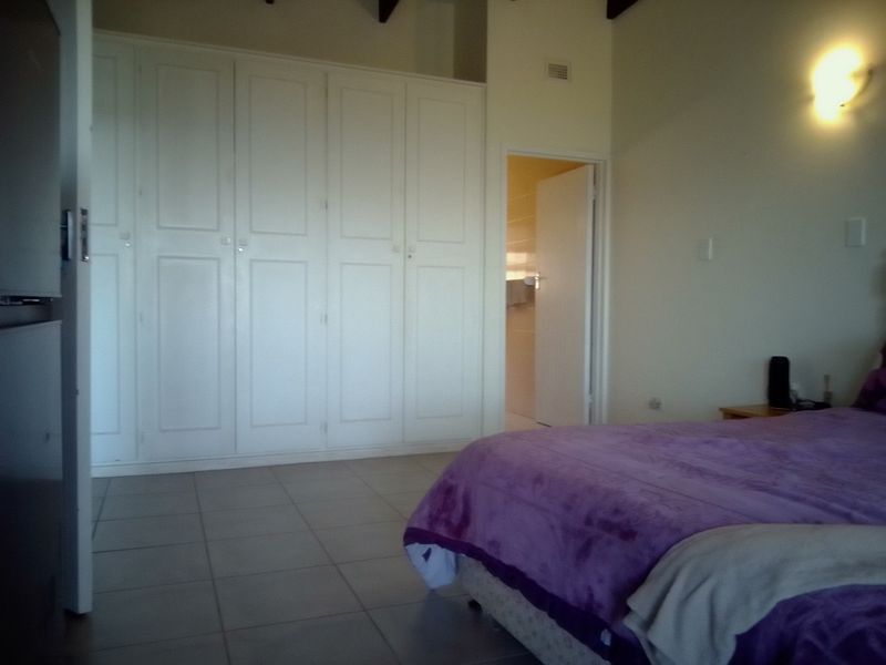 A bedroom featuring built-in cupboards, tiled flooring, and exposed ceiling beams, with an adjoining bathroom visible through the doorway.