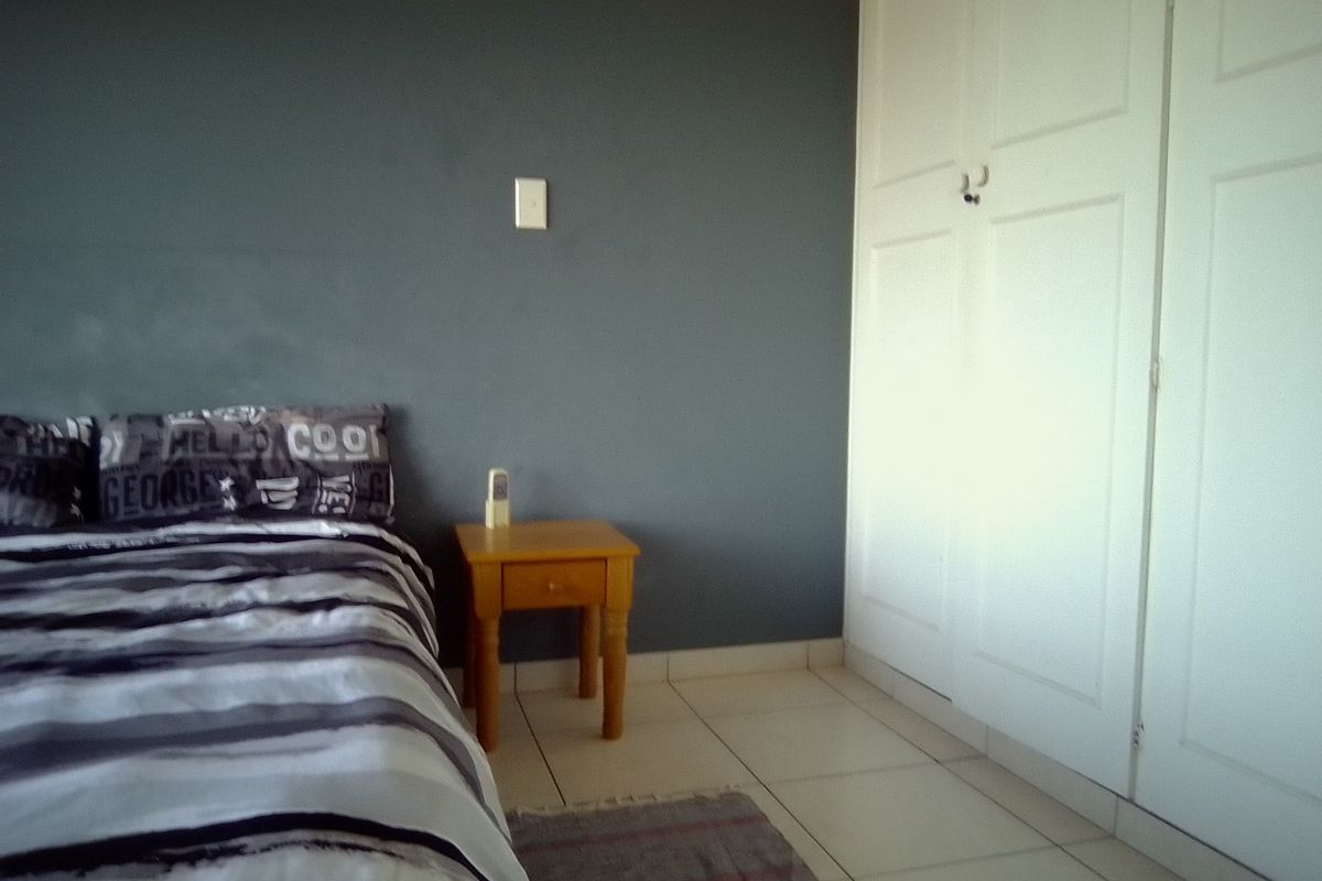 A bedroom featuring tiled flooring, a dark accent wall, and built-in white cupboards providing ample storage space.