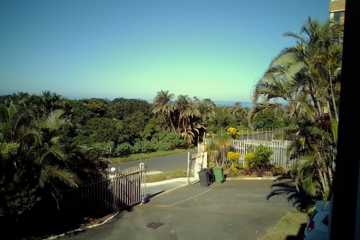 Elevated view overlooking the property entrance, driveway, and surrounding lush coastal landscape with distant ocean horizon.