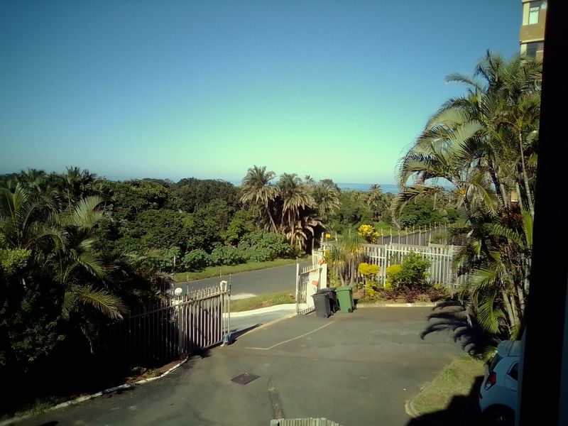 Elevated view overlooking the property entrance, driveway, and surrounding lush coastal landscape with distant ocean horizon.