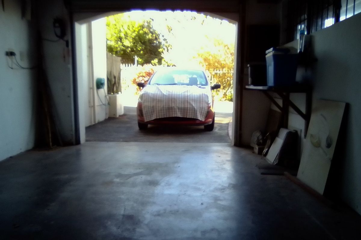 A view from inside a garage looking out towards the driveway, featuring concrete flooring and basic wall-mounted storage shelving.