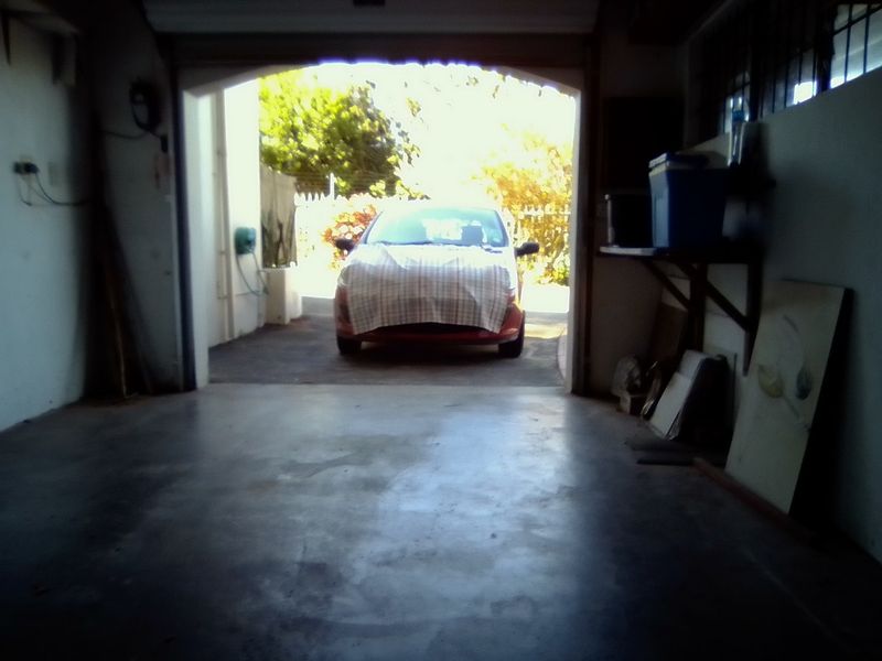 A view from inside a garage looking out towards the driveway, featuring concrete flooring and basic wall-mounted storage shelving.