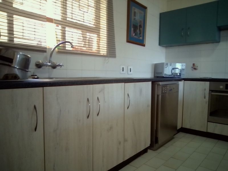 A functional kitchen featuring light wood-look cabinetry, dark laminate countertops, tiled backsplash, and integrated oven, offering a clean and practical workspace.