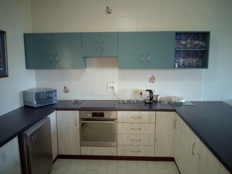 A functional kitchen featuring a U-shaped layout with light wood-finish lower cabinets, blue upper cabinets, a built-in oven, and a tiled backsplash.