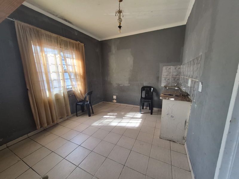 A compact kitchen area featuring tiled flooring, a basic sink unit, and tiled splashbacks, currently requiring cosmetic updates and wall repairs.