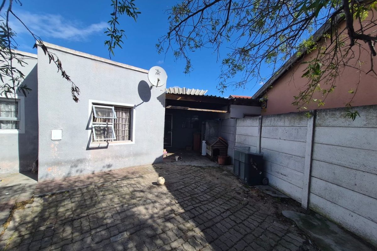 A rear courtyard featuring paved flooring, a precast concrete boundary wall, and a small covered patio area attached to the main dwelling.